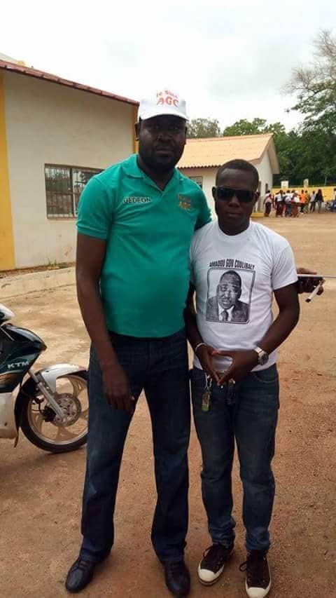 Molo Kanté, portant un tee-shirt à l'effigie du premier ministre Amadou Gon Coulibaly, et posant à côté du responsable RJR Korhogo